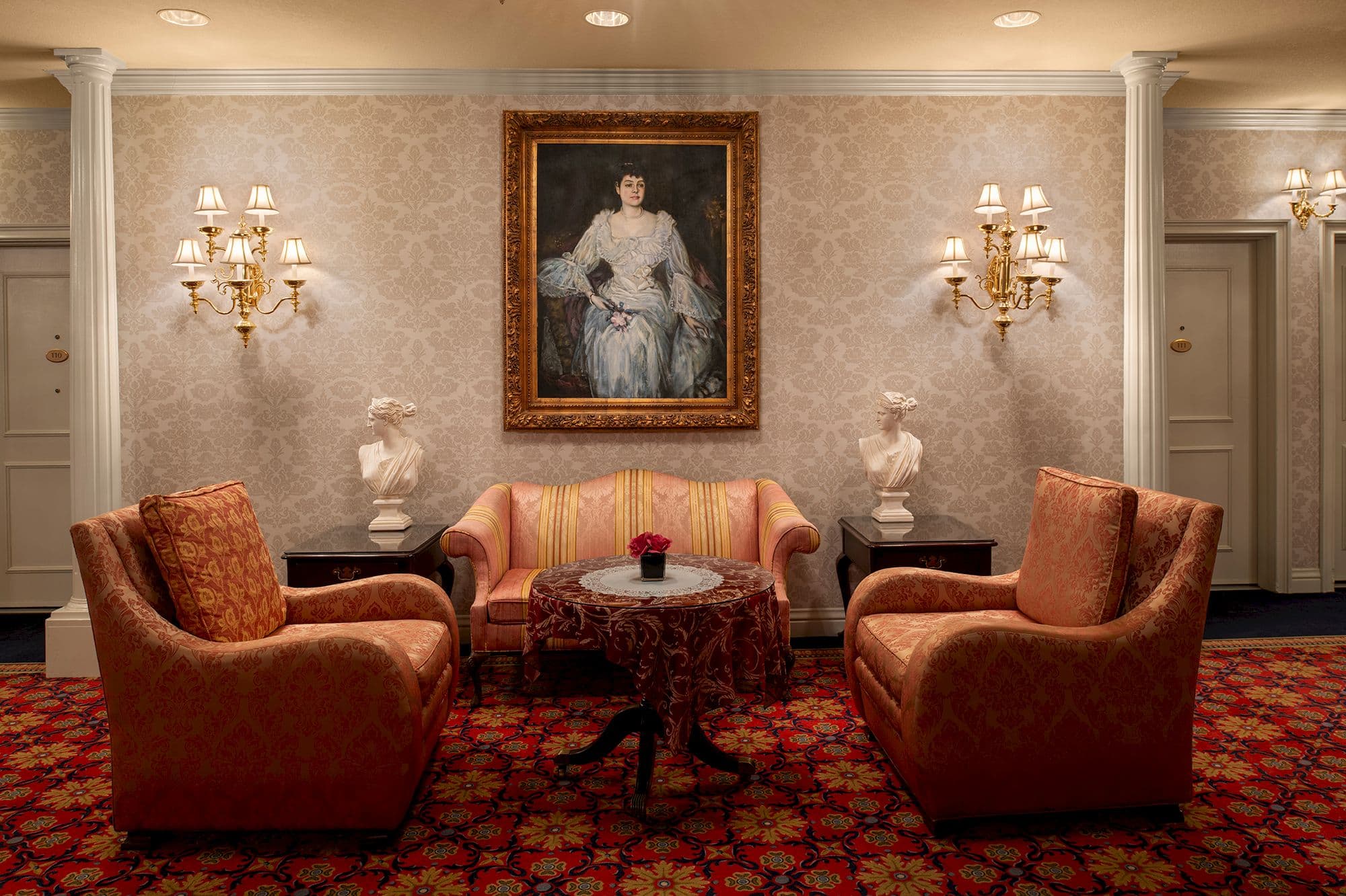 Sitting area with a striped settee, two armchairs and a portrait between brass sconces